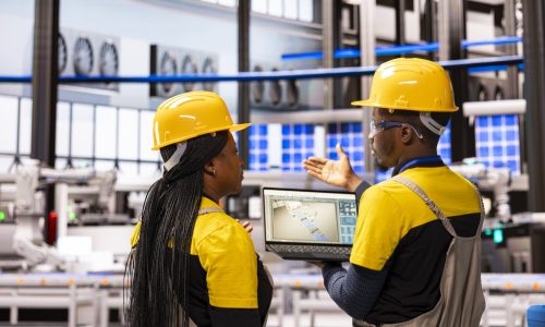 Black team of engineers supervising smart manufacturing process using digital interface on laptop. Robotic arms and automation assembly lines streamline industrial production for enhanced efficiency.
