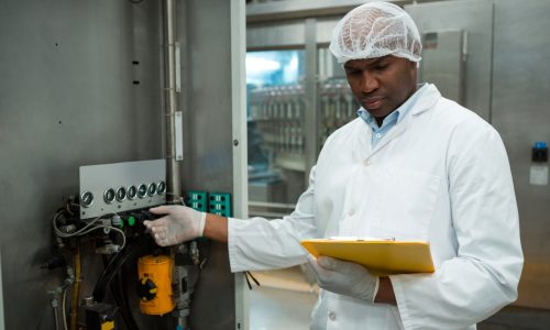 Confident male worker holding clipboard while operating machine in juice factory